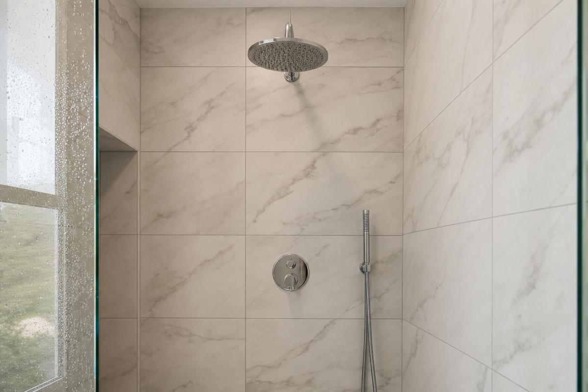 Ducha nueva con paredes de porcelanato marmolado y grifería cromada